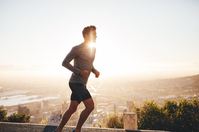 Young man training in the nature with sun behind him. Young man on morning run outdoors.